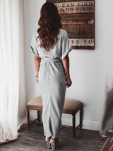 Back view of a woman wearing a light gray satin maxi dress with short sleeves and a tie waist.