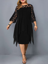 Plus-size woman wearing a black layered dress with geometric mesh sleeves and an asymmetrical hemline, standing against a grey background.