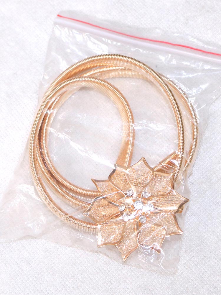 Close-up of a gold elastic belt with a floral embellishment and rhinestones, packaged in plastic.