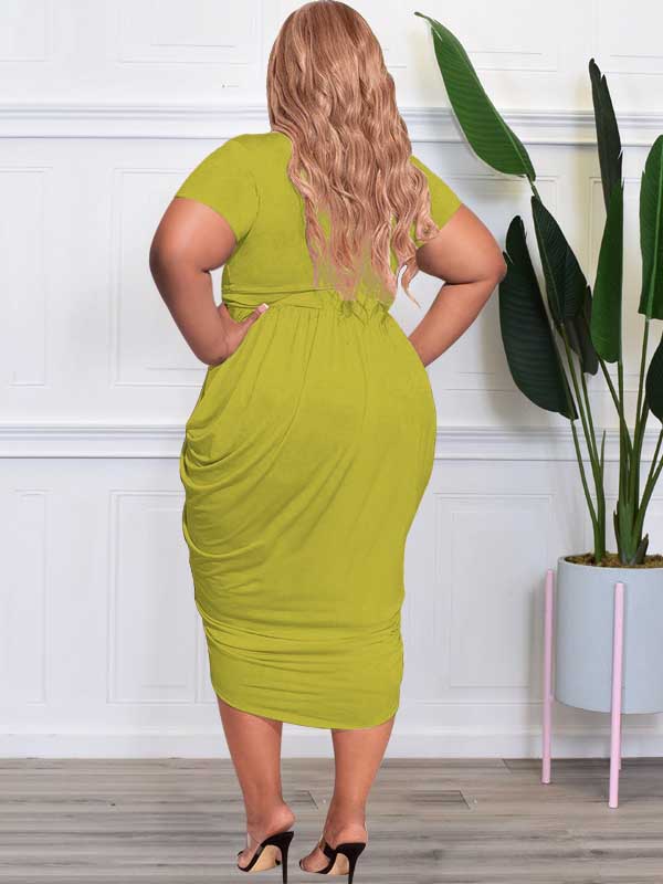 Plus-size model wearing a royal blue ruched V-neck short-sleeve dress with a tulip hem, side slit, and a gold double-ring belt, paired with pink strappy heels.