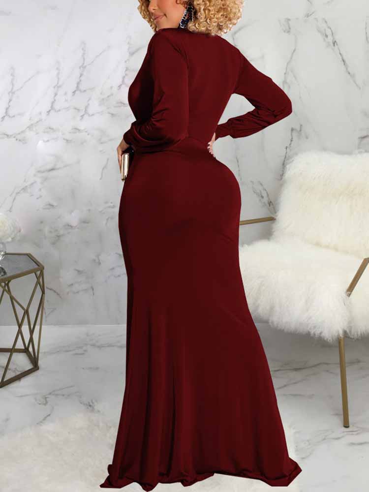 Back view of a woman wearing a long burgundy dress with a deep V-neckline, long sleeves, ruched detailing, and a high slit.