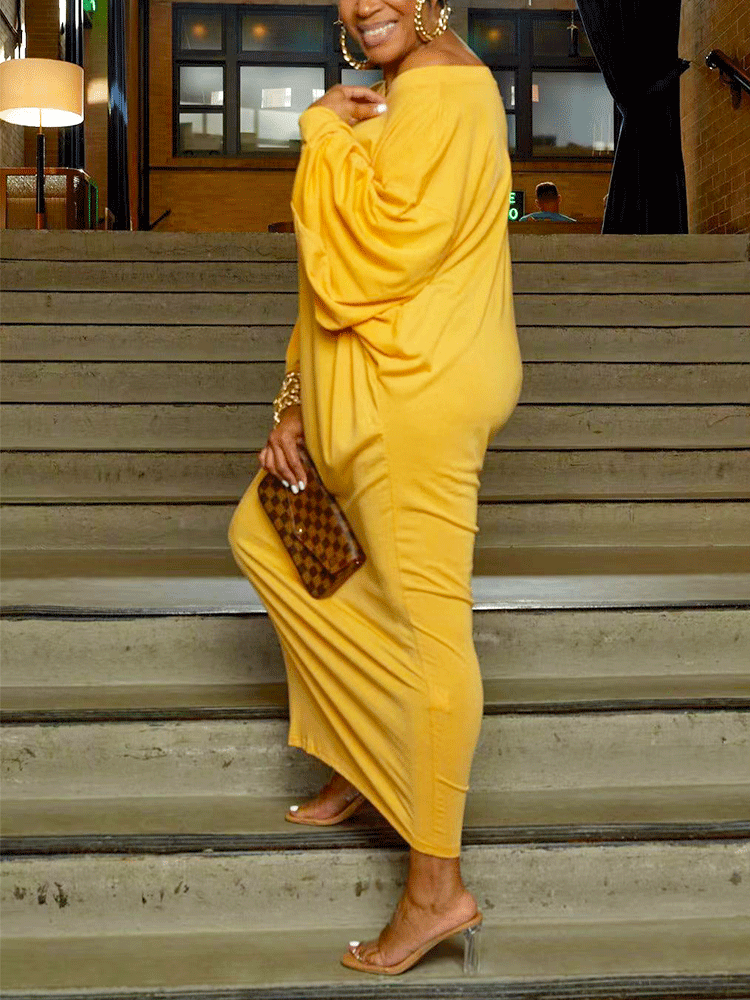 Side view of a woman in a yellow off-the-shoulder maxi dress with balloon sleeves, standing on stairs.