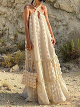 Woman wearing a cream-colored maxi dress with a halter neckline and tiered skirt in an outdoor desert setting.