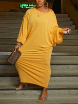 Woman wearing a yellow off-the-shoulder maxi dress with balloon sleeves and clear heels, holding a checkered clutch.