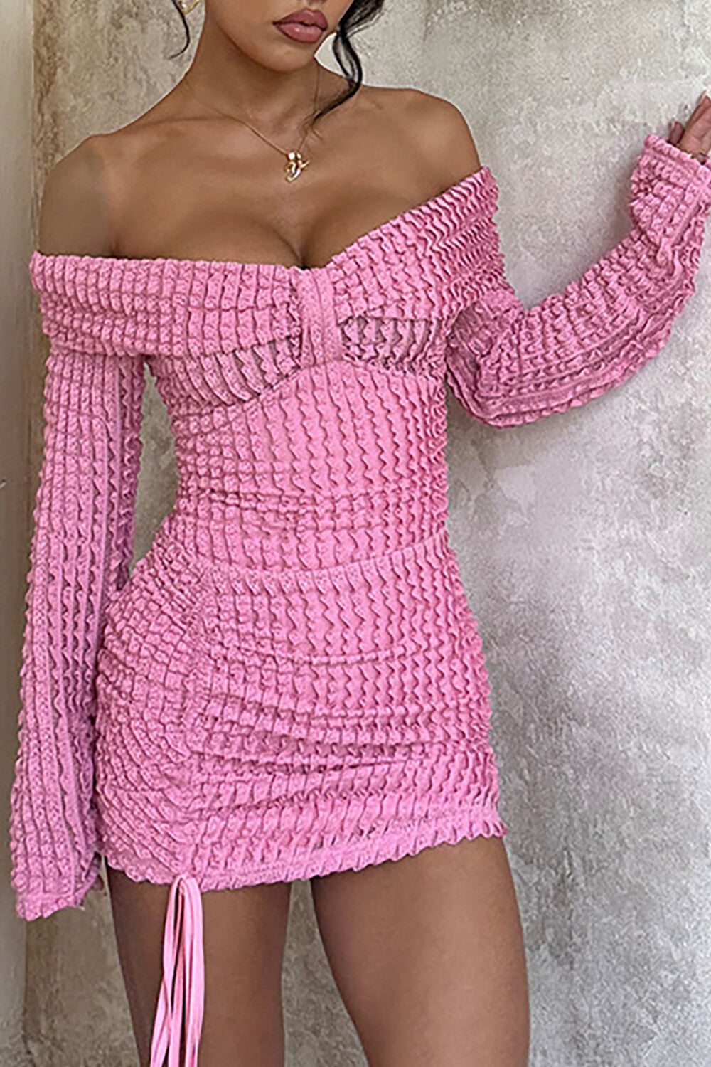 Close-up of a pink off-the-shoulder ruched knit mini dress with long sleeves.