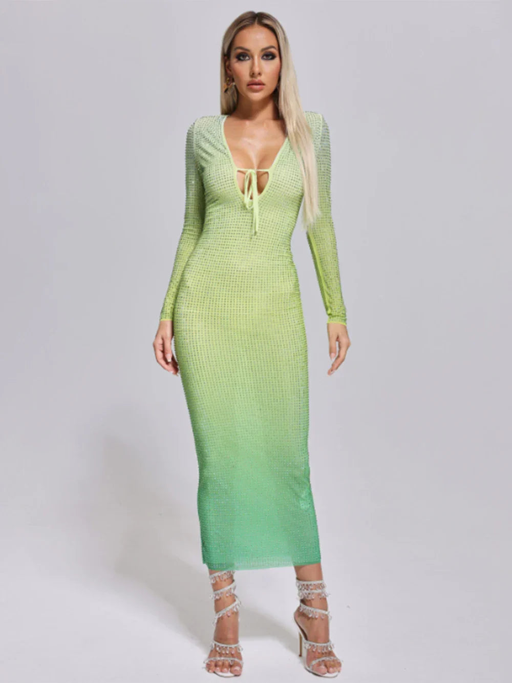 Woman wearing a long, form-fitting, gradient green dress with long sleeves and a plunging neckline adorned with rhinestones.