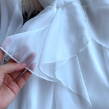 Hand touching the sheer ruffled layer of a white dress