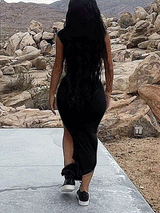 Rear view of a woman wearing a black one-shoulder, draped maxi dress with a high slit and sneakers, walking away.