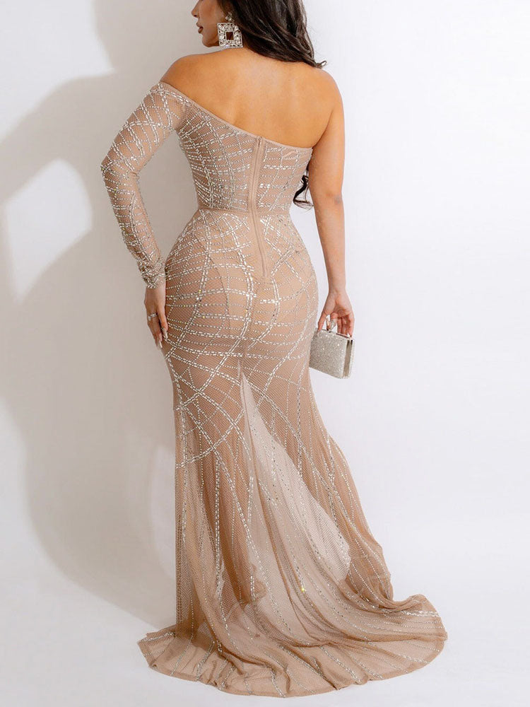 Back view of a woman in a nude, off-the-shoulder, floor-length gown with a high slit and silver embellishments, holding a silver clutch.