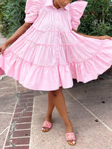 Close-up of a woman wearing a pink tiered puff sleeve collared dress, showing the ruffles and tiered skirt.