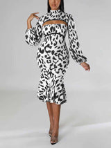 Woman wearing a black and white leopard print knit dress with a high neck, cut-out detail, long puff sleeves, and a mermaid hemline, posing with one hand on her hip.