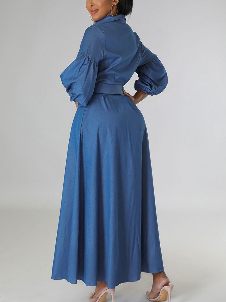 Back view of a woman in a blue denim maxi dress with puffed sleeves and a belted waist.