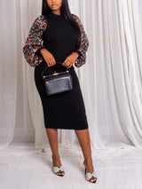 Woman wearing a black midi dress with sequined balloon sleeves, holding a black handbag.