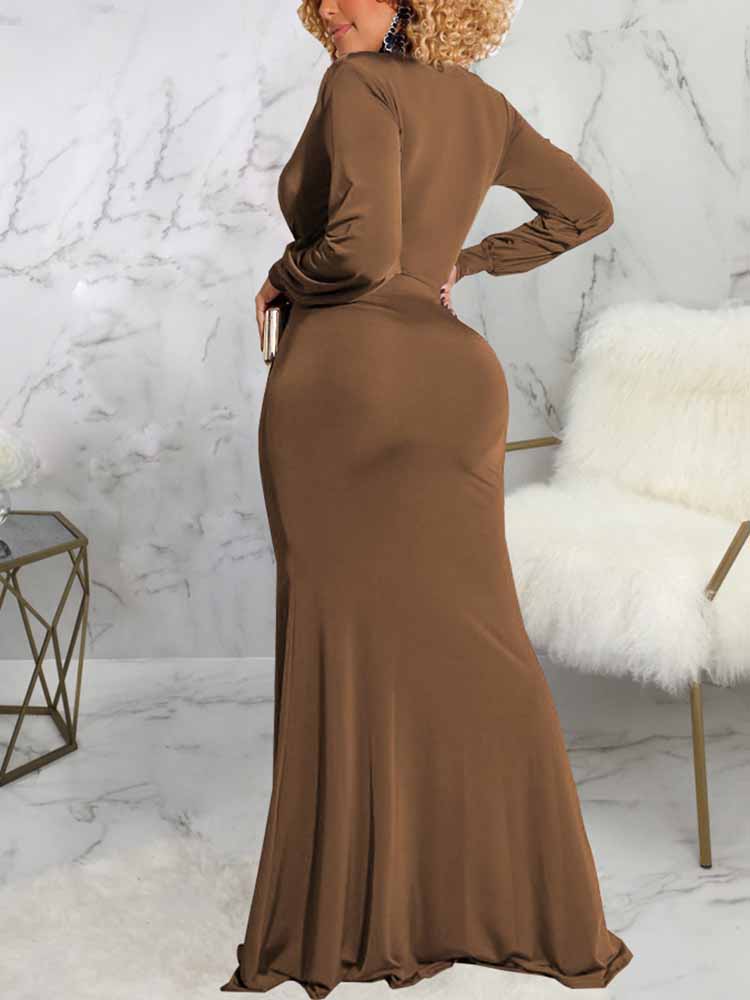 Back view of a woman wearing a long brown dress with a deep V-neckline, long sleeves, ruched detailing, and a high slit.