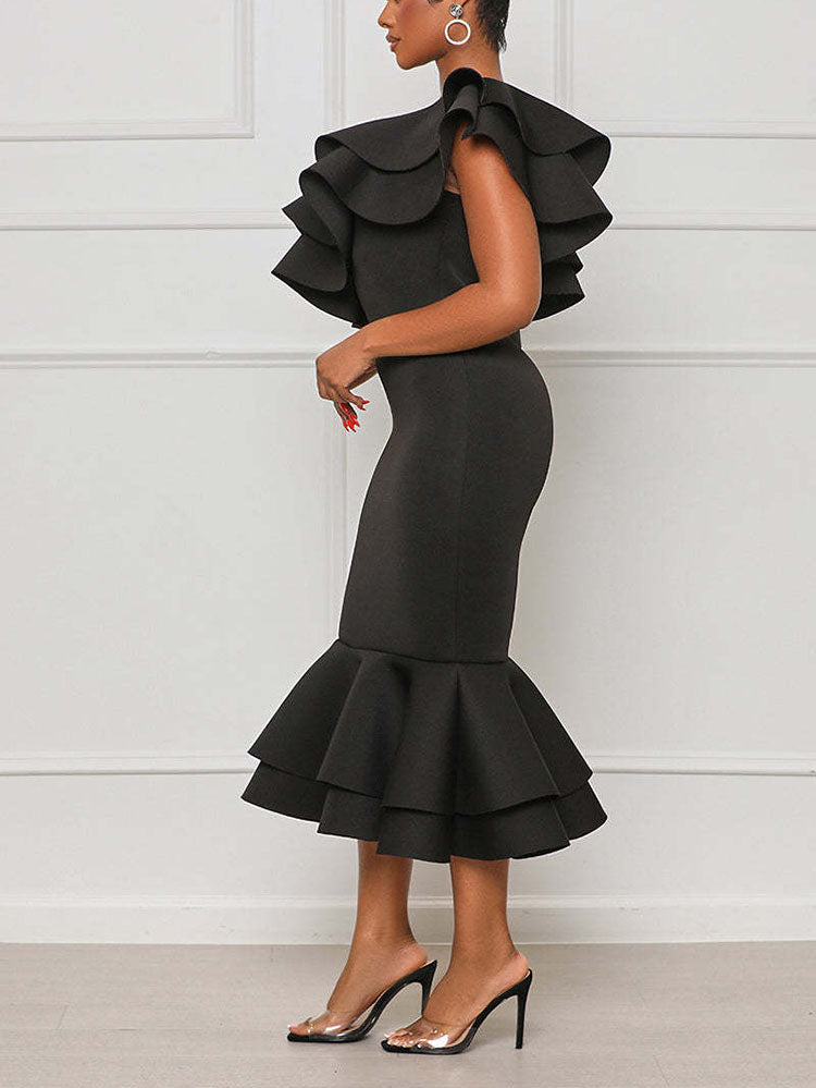Side view of a woman in a black one-shoulder midi dress with ruffle details and a mermaid hem.