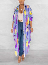 Woman wearing a long, light purple collared shirt dress with a colorful graphic print of people, open over jeans and a tank top.