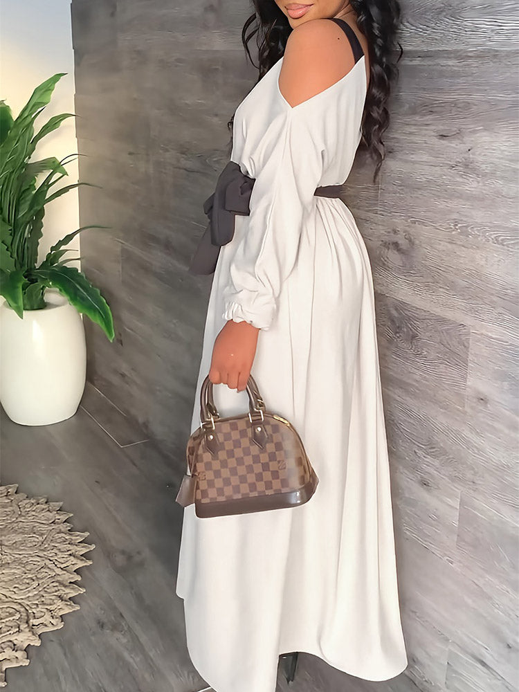 Side view of a woman in a long, off-the-shoulder white dress with a black tie-waist belt, holding a handbag.