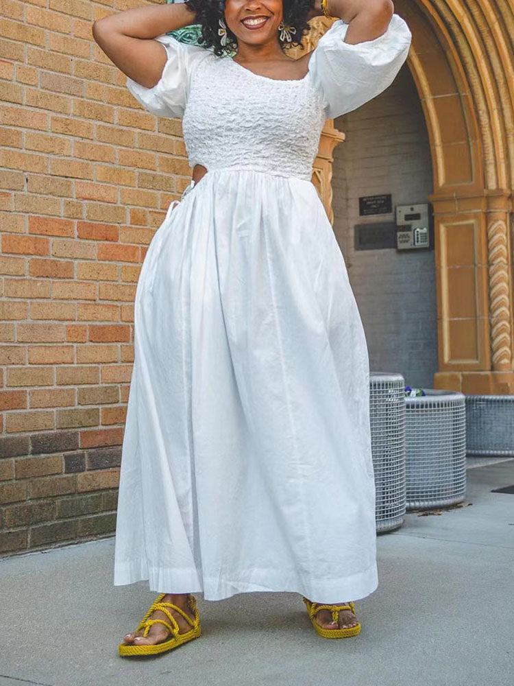 Woman in a white one-shoulder maxi dress with smocked bodice and puff sleeves, standing outdoors.