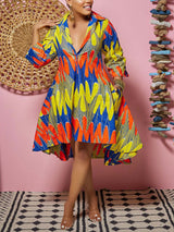 Woman wearing a colorful printed high-low dress with 3/4 sleeves and pockets, standing against a pink background.