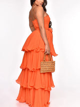 Side view of a woman in an orange tiered maxi dress with spaghetti straps.