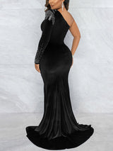 Woman wearing a royal blue one-shoulder velvet gown with a sheer illusion panel and high slit