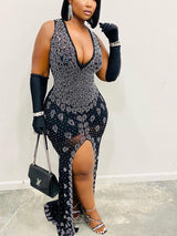 Woman in a black sleeveless mermaid gown with a deep V-neckline and high slit, adorned with rhinestones.