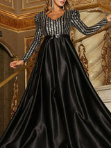Woman wearing a black long-sleeved A-line formal dress with a sequined striped bodice and a satin skirt.