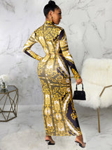 Back view of a woman in a long-sleeved, baroque-print maxi dress with a high neckline and a belted waist.