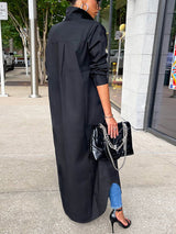 Back view of a woman wearing a long black button-down shirt dress with blue jeans and black high heels