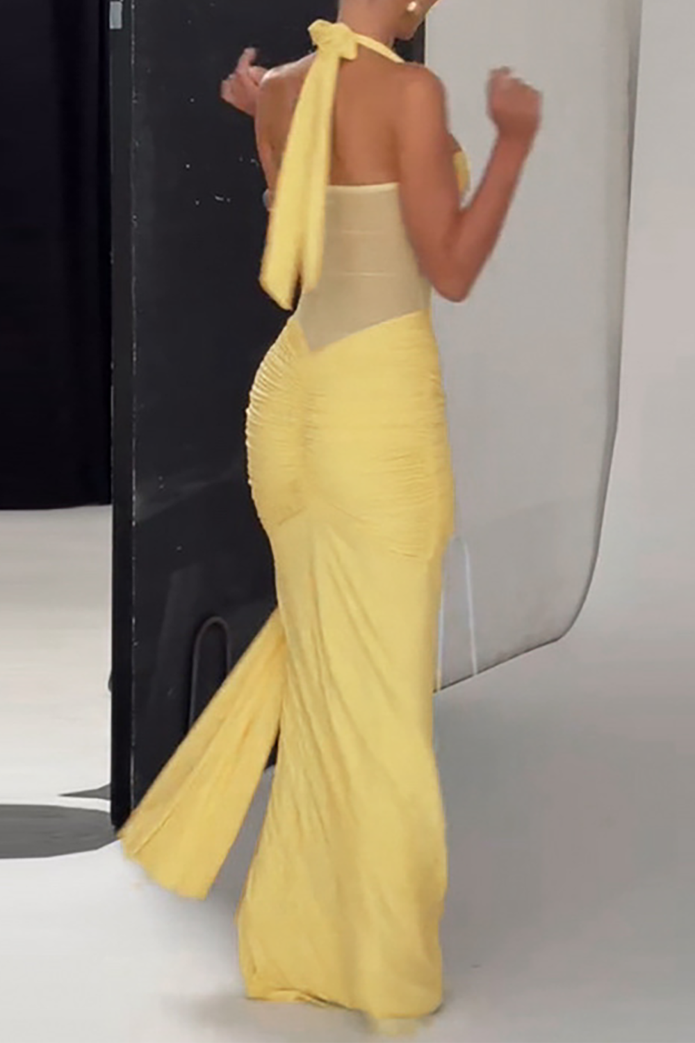 Woman wearing a floor-length yellow halter dress with ruched detailing and a sheer bodice, back view