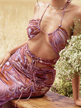 Woman wearing a marble print halter neck dress with cut-out detailing and ruched skirt, sitting outdoors.