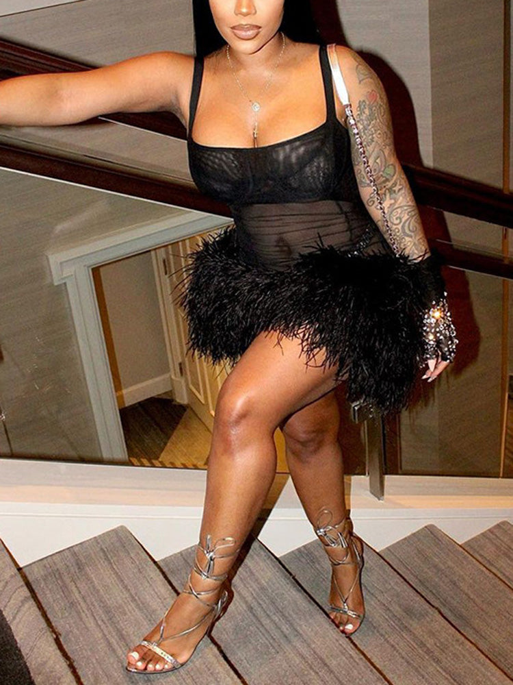 Close-up of a woman's legs and torso in a black mini dress with feather trim, wearing strappy heels.