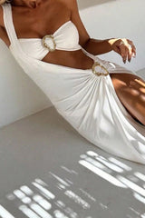 Woman wearing a white one-shoulder maxi dress with a high slit and gold-tone hardware accents.
