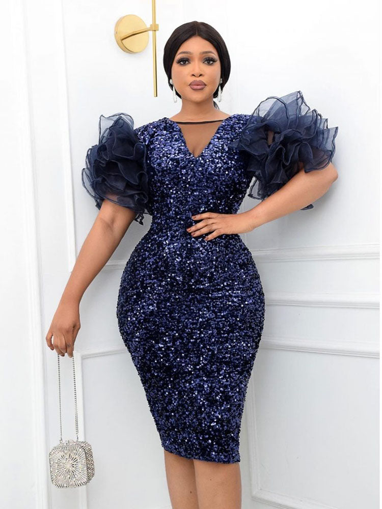 Woman in a navy blue sequined dress with voluminous sheer sleeves, holding a silver clutch.