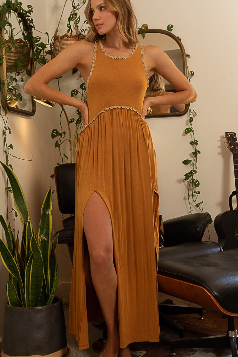 Woman in a rust-colored maxi dress with high leg slits and a lace-trimmed neckline, with hands on her hips.