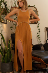 Woman in a rust-colored maxi dress with high leg slits and a lace-trimmed neckline, with hands on her hips.