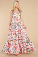 A woman in a flowing floral maxi dress with layered tiers and bow shoulder straps.