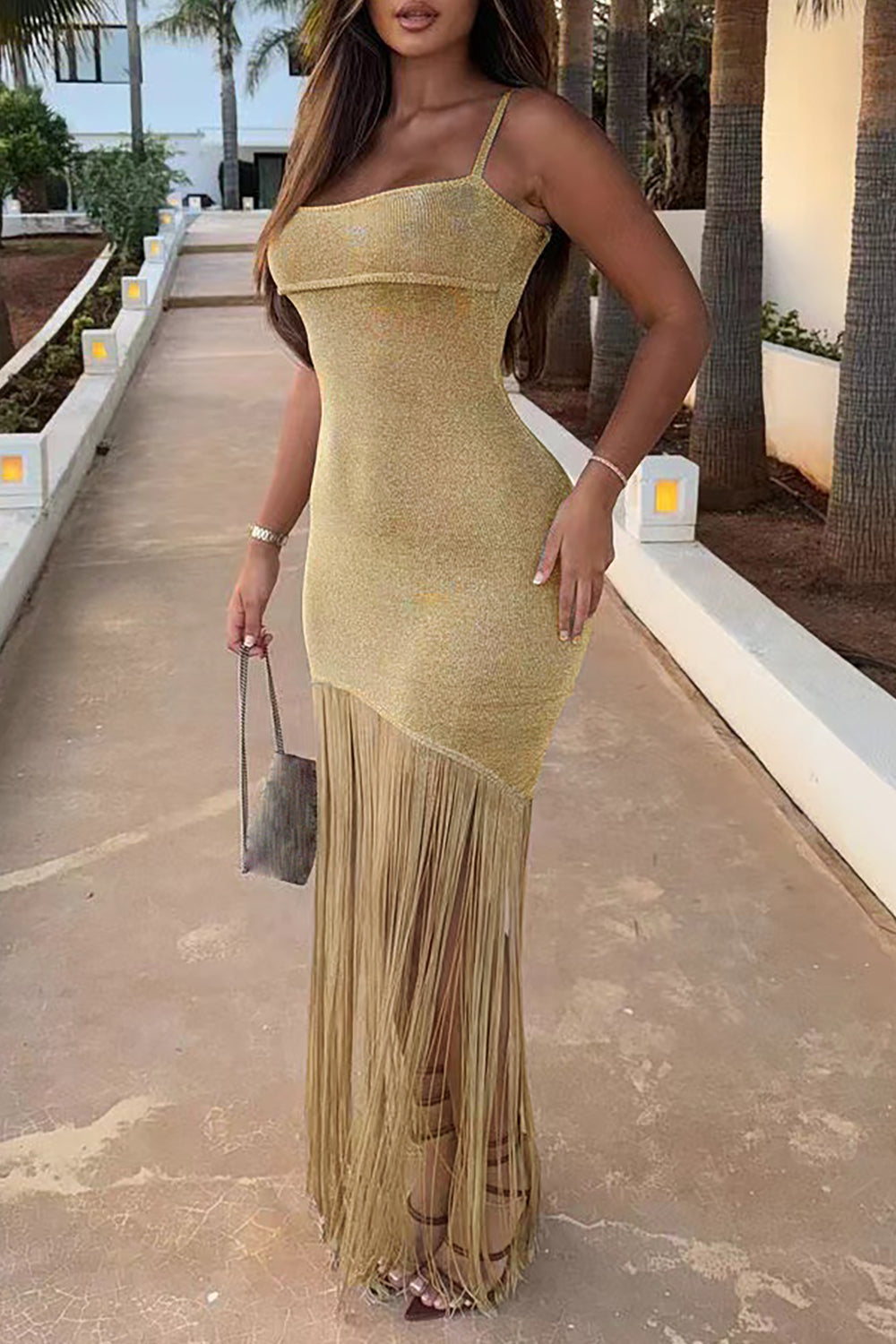 Woman in a gold sparkly maxi dress with fringe and a high slit, outdoors