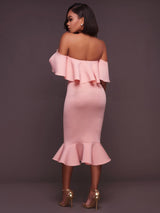 Woman wearing a pink off-the-shoulder ruffle dress and gold heels, back view