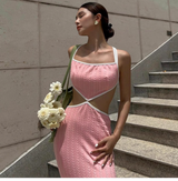 Woman wearing a pink knit midi dress with cut-out details and a green mesh bag with flowers, standing on stairs.