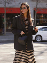 Woman wearing a black blazer over a knit dress with a black and beige geometric diamond pattern, carrying a heart-shaped black handbag.