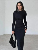 Woman wearing a long-sleeved, ruched, black maxi dress and holding a black handbag.