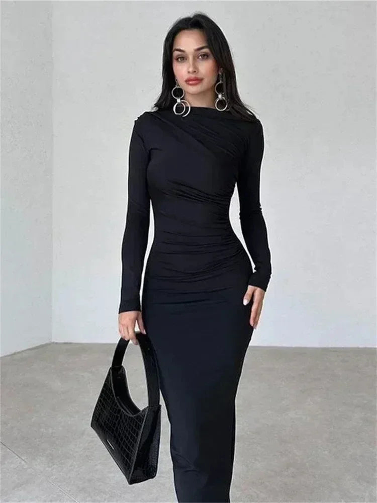 Woman wearing a long-sleeved, ruched, black maxi dress and holding a black handbag.