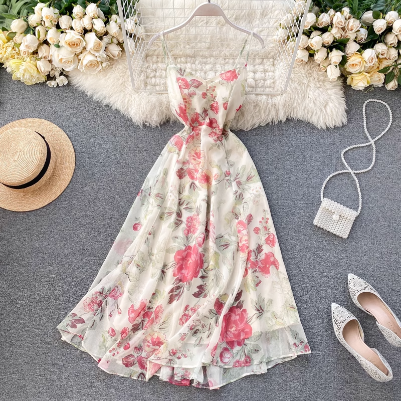 A floral print midi dress with spaghetti straps and a V-neckline laid flat on a grey surface, surrounded by flowers and accessories.