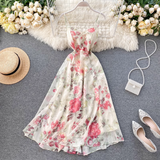 A floral print midi dress with spaghetti straps and a V-neckline laid flat on a grey surface, surrounded by flowers and accessories.