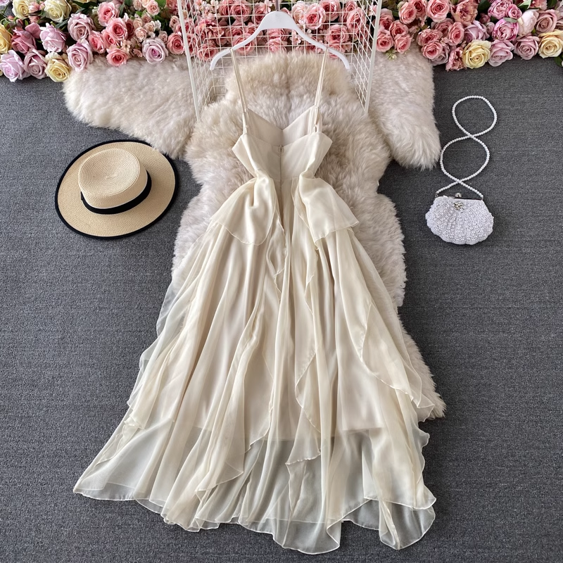Back view of a cream-colored chiffon dress with ruffle detailing and spaghetti straps, laid flat on a faux fur rug.