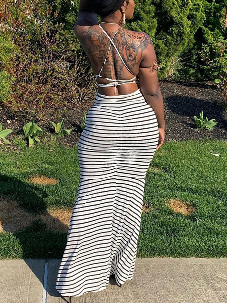 Back view of a woman in a black and white striped maxi dress, highlighting the intricate strap detail on the open back and the fishtail hem.