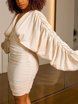 Side view of a woman in a cream-colored ruched bodycon dress, showcasing the fit and sleeve design.