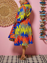 Woman showing the back of a colorful printed high-low dress with 3/4 sleeves and pockets.