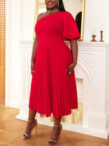 Woman posing in a red one-shoulder pleated dress and gold heels.